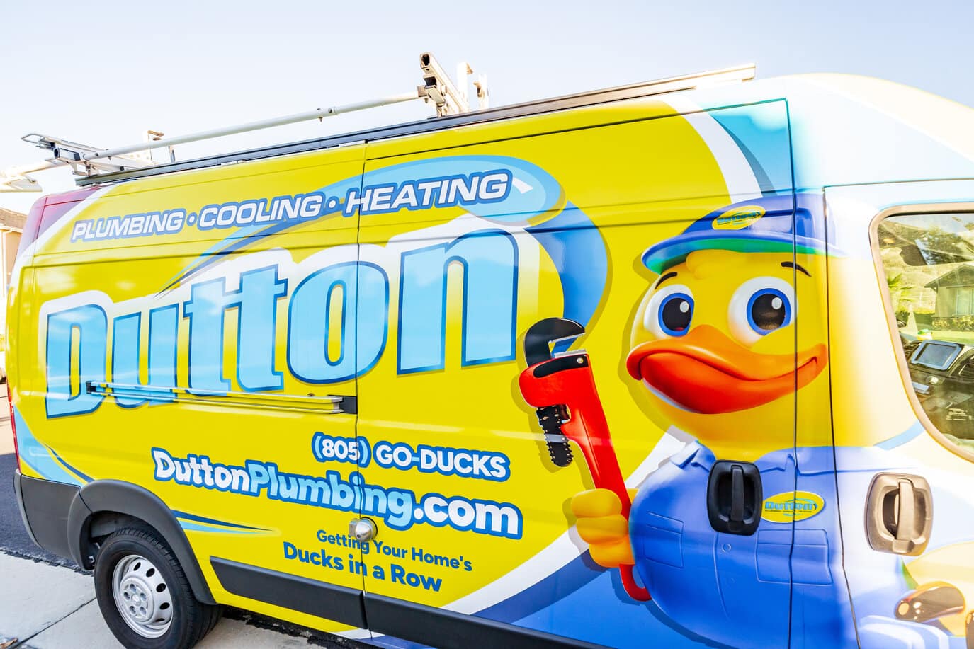 Bright yellow Dutton Plumbing service van with duck mascot holding a red wrench, plumbing cooling heating branding