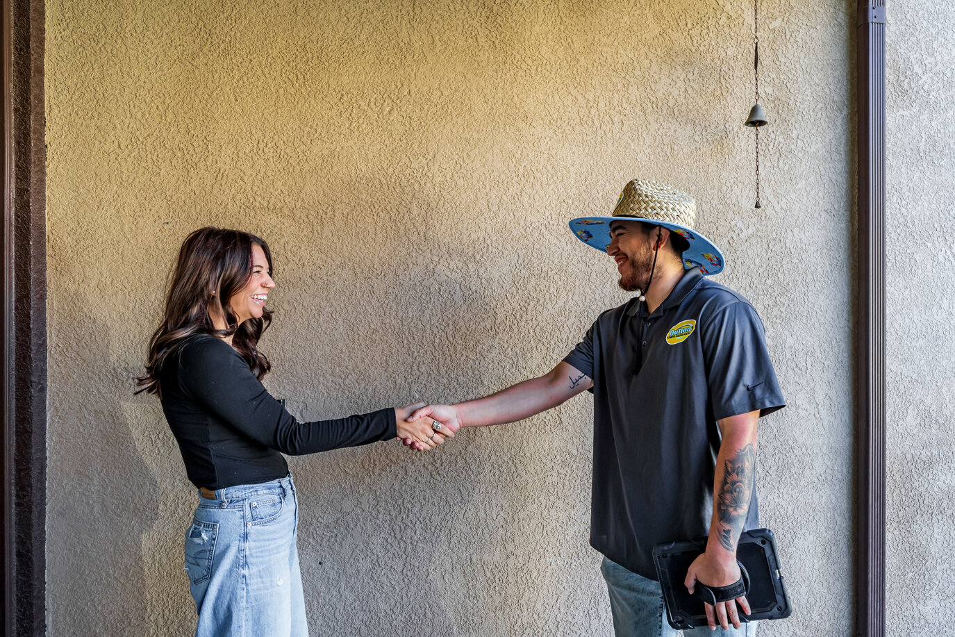 Woman shaking hands with a smiling service technician in a straw hat holding a tablet