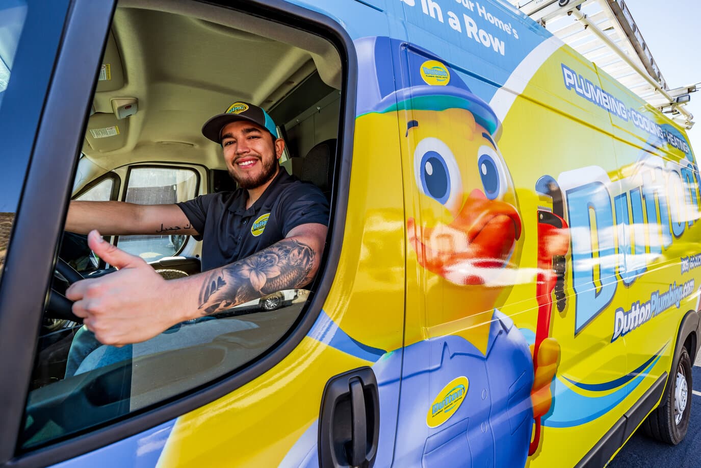 Plumber smiling and giving thumbs up from driver's window of bright Dutton Plumbing service van