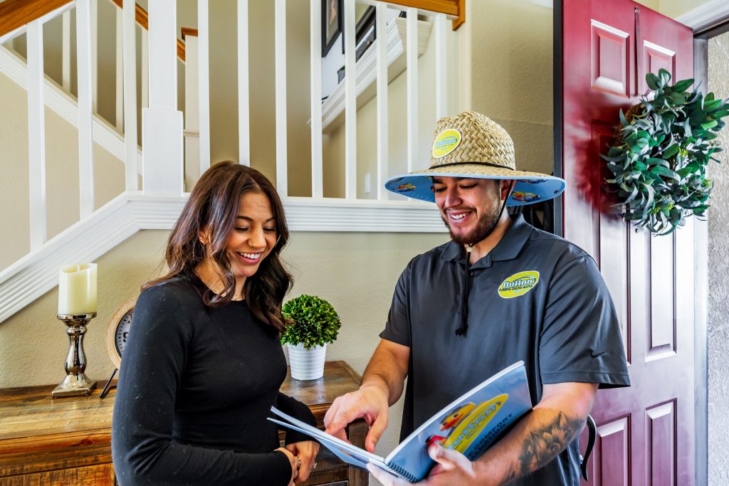 Technician in branded shirt and straw hat reviewing a brochure with a woman during a home service visit.