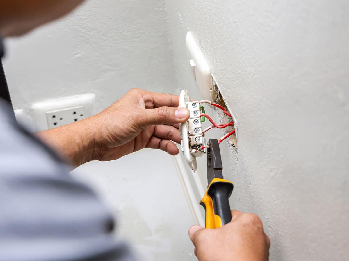 An electrician repairing wall outlet wiring with pliers