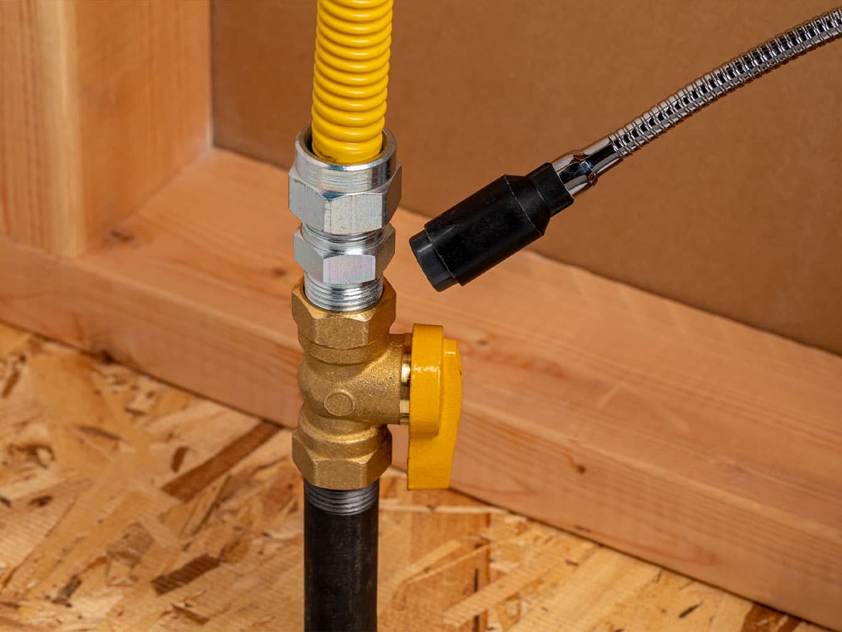 Brass gas shutoff ball valve with yellow handle and corrugated yellow gas line on plywood floor