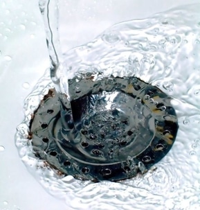 Close-up of a stainless steel sink drain with water pouring and splashing around it