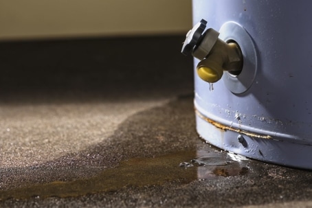 Leaking water heater spigot with rust and water pooling on concrete floor