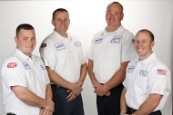 Four technicians in white work shirts with name patches smiling and standing against a white background.