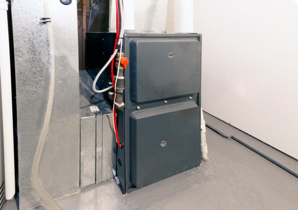 An HVAC furnace/air handler with ductwork, red and white lines, and condensate piping in a finished basement utility room