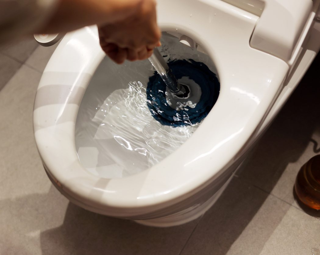 A person plunging a toilet with a blue-rimmed plunger, water swirling in the bowl.