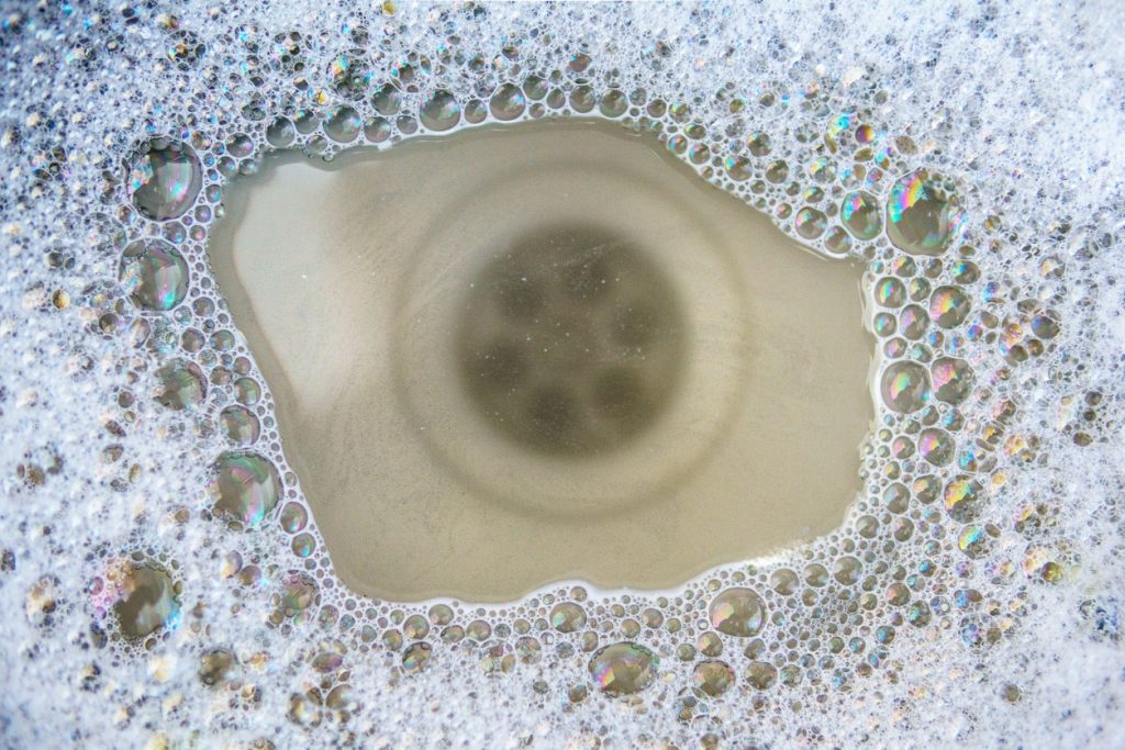 Top-down view of a sink drain surrounded by soapy bubbles with iridescent reflections