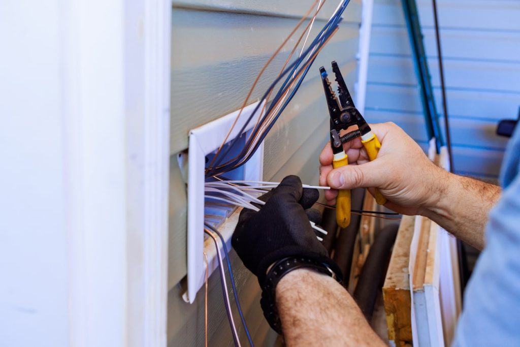 Person stripping and organizing outdoor electrical wires at a house exterior using a wire stripper