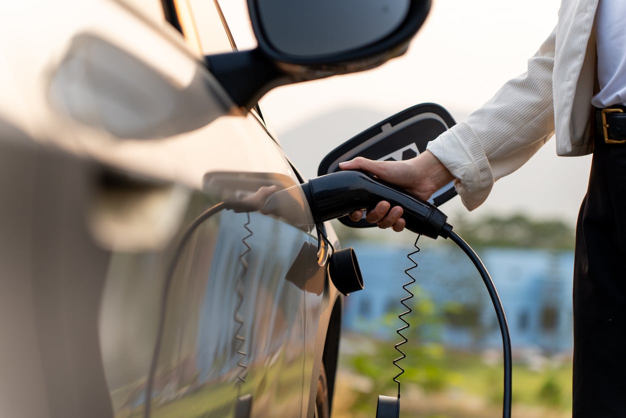 A person plugging an EV charging cable into an electric car at an outdoor charging station