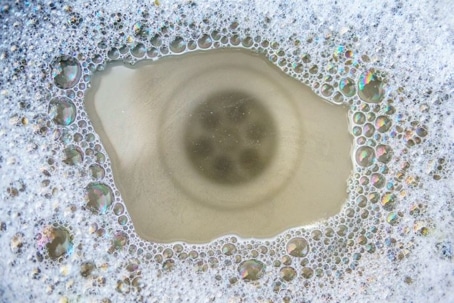 Close-up of a kitchen sink drain surrounded by soapy, iridescent dish bubbles