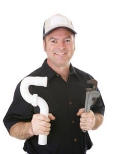 Smiling plumber in cap holding PVC pipe elbow and pipe wrench on white background